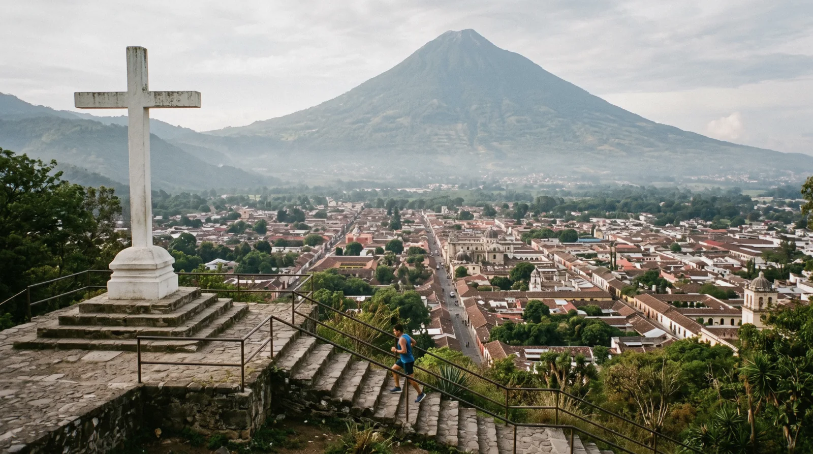 The white cross on Cerro de la Cruz above Antigua Guatemala, the whole colonial grid below with Volcan de Agua rising behind, one jogger on the steps