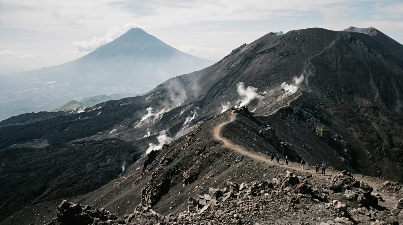 Visitors crossing the black lava fields below Pacaya volcano, steam rising from vents under a grey cone